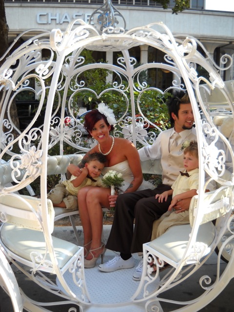 A bride and groom sitting in a white gazebo with their children.