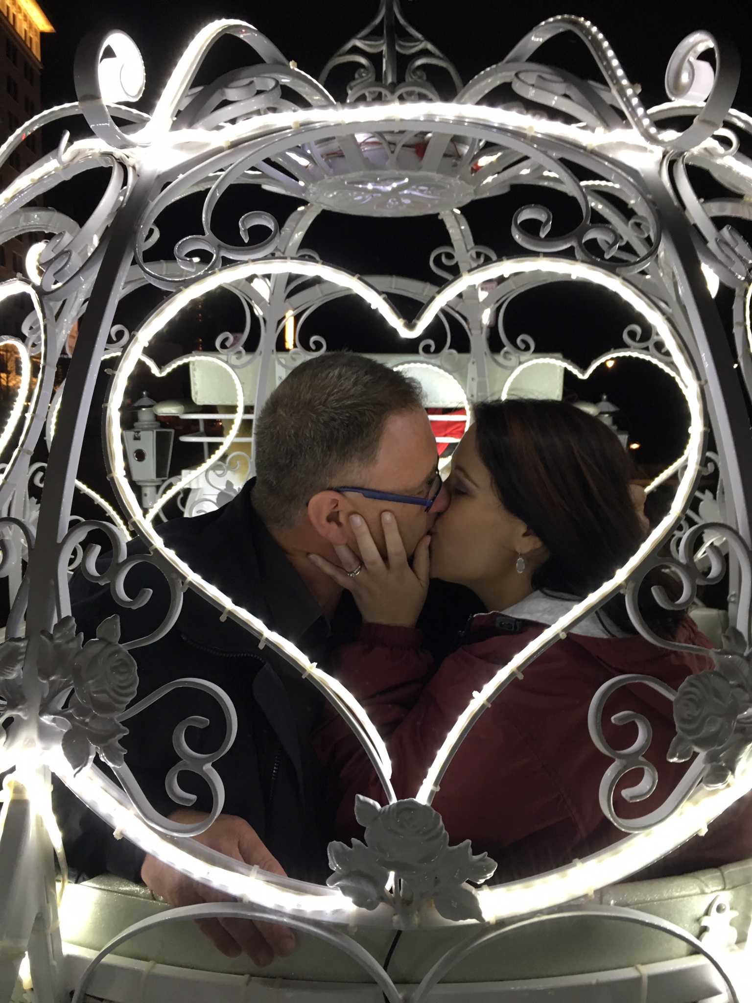 A man and woman kissing in front of a heart shaped gate.
