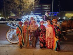 Group in colorful costumes by lit carriage.