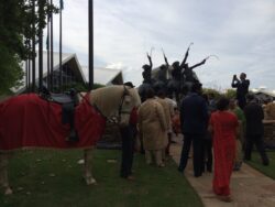People gathering near statue with horse present.